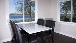 Un comedor con mesa y sillas, ventanas amplias con vistas a un lago y árboles.