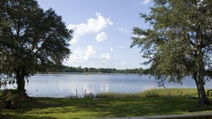 Vista a la orilla de un lago con muelle de madera, árboles y agua tranquila.