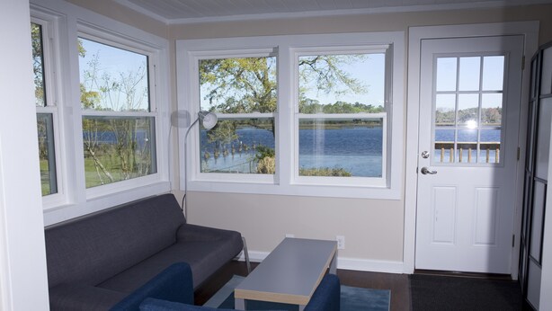 Una habitación con un sofá gris, una mesita y vista a un lago a través de amplias ventanas.