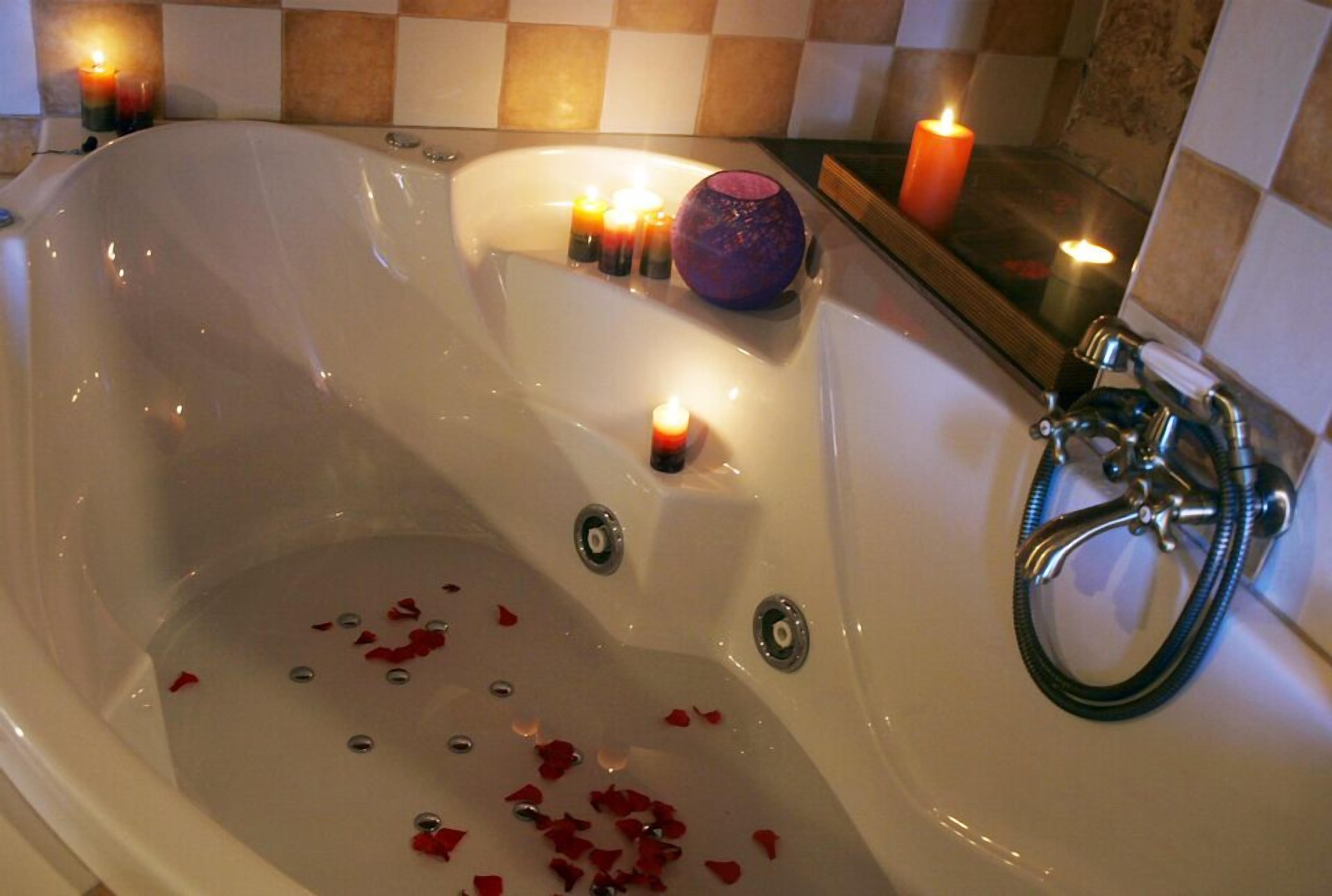 Una bañera con pétalos de rosa, velas y un jarrón morado.