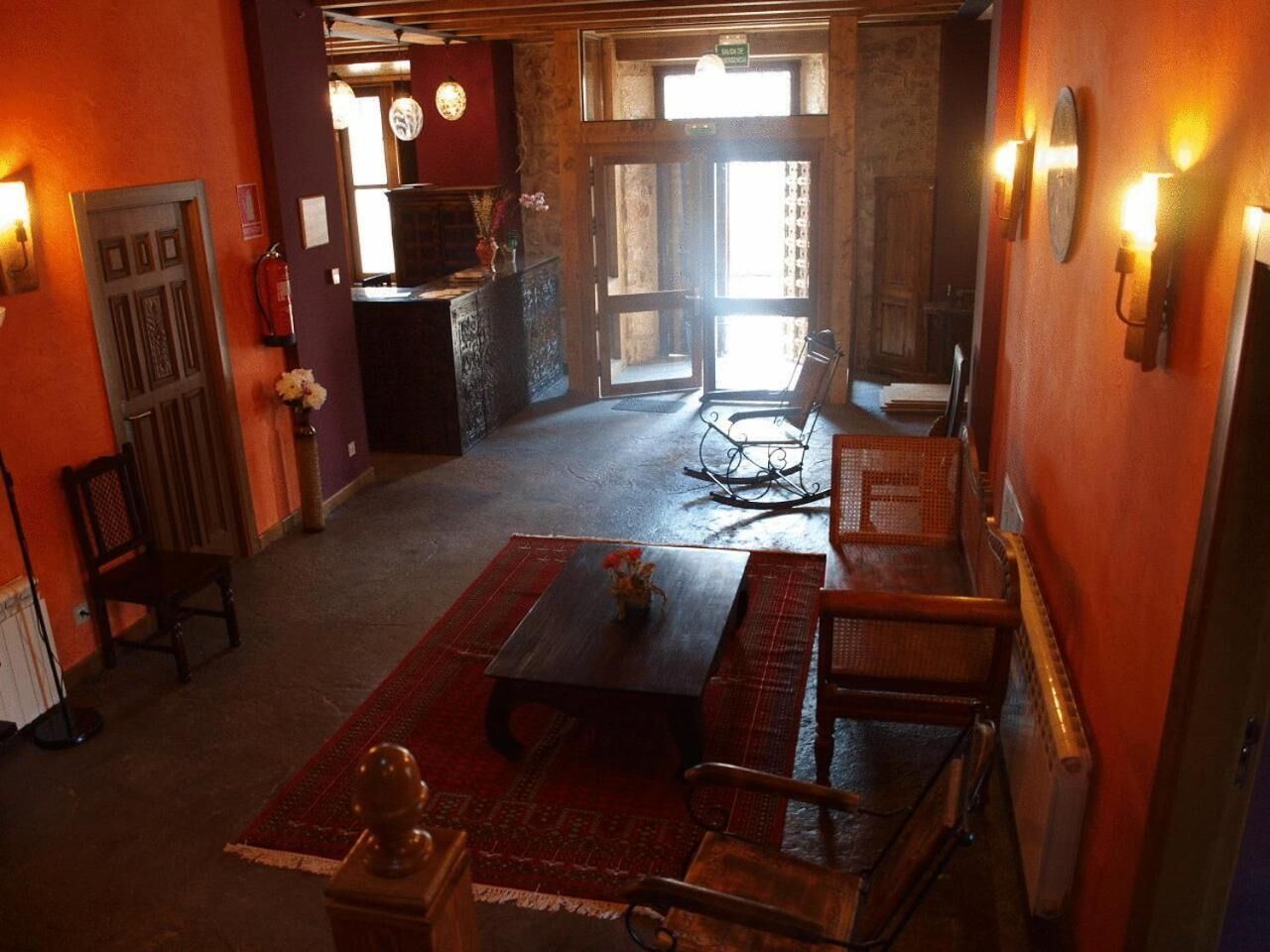 Un interior acogedor con una mesa de madera, sillas y una alfombra roja. Una puerta da a una zona de cocina con una estufa y una ventana.