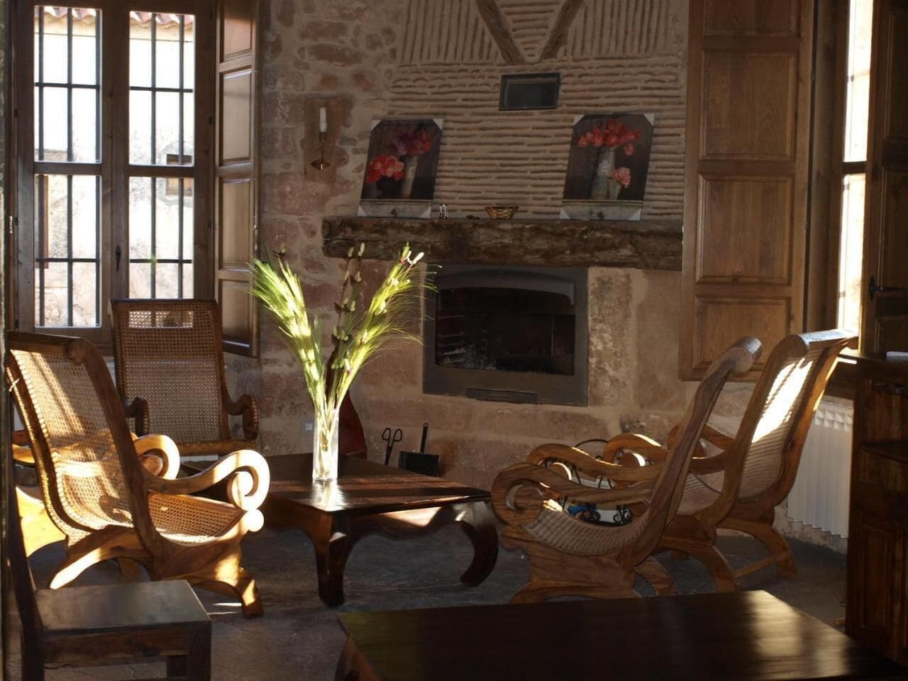 Una habitación rústica con chimenea de piedra, muebles de madera y un jarrón con plantas.