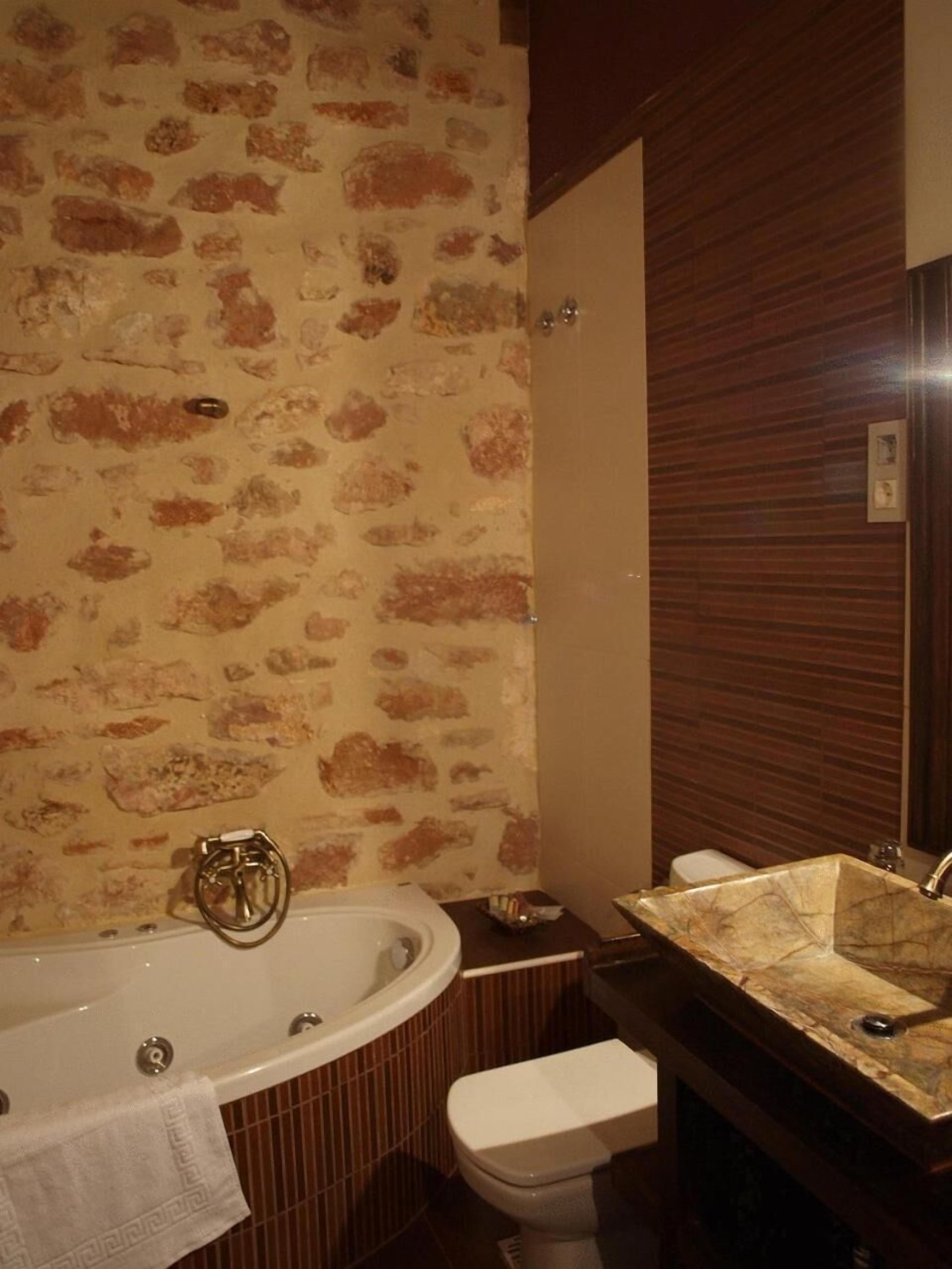 Un baño con pared de diseño de piedra, una bañera independiente, un lavamanos con encimera de mármol y un inodoro.