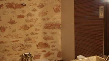 Un baño con pared de diseño de piedra, una bañera independiente, un lavamanos con encimera de mármol y un inodoro.