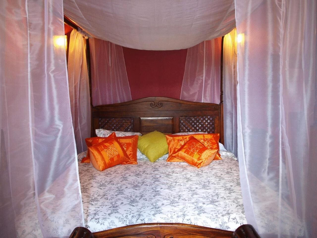 Una cama con colcha estampada con flores, almohadas naranjas y amarillas, y un cabecero de madera.