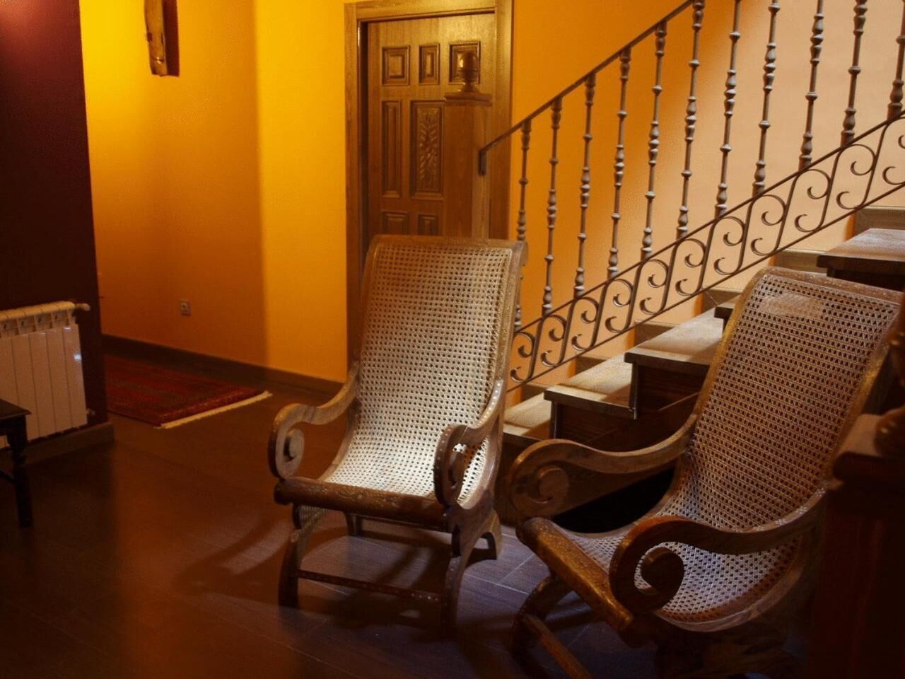 Una silla de madera con respaldo trenzado en una habitación con suelo de madera y una escalera con barandilla de hierro forjado.