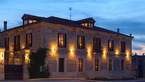 A stone building with multiple windows and a gated entrance, illuminated by exterior lights. - Posada Real El Señorío de la Serrezuela (Aldeanueva De La Serrezuela)
