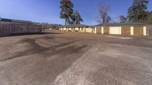 A parking lot with a row of buildings, including a fenced area and a building with a patterned wall. - OYO Hotel Brookhaven MS Hwy 51 North (Brookhaven)