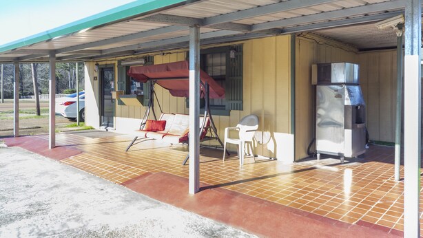 A covered outdoor seating area with a swing chair, a small table, and a refrigerator. - OYO Hotel Brookhaven MS Hwy 51 North (Brookhaven)