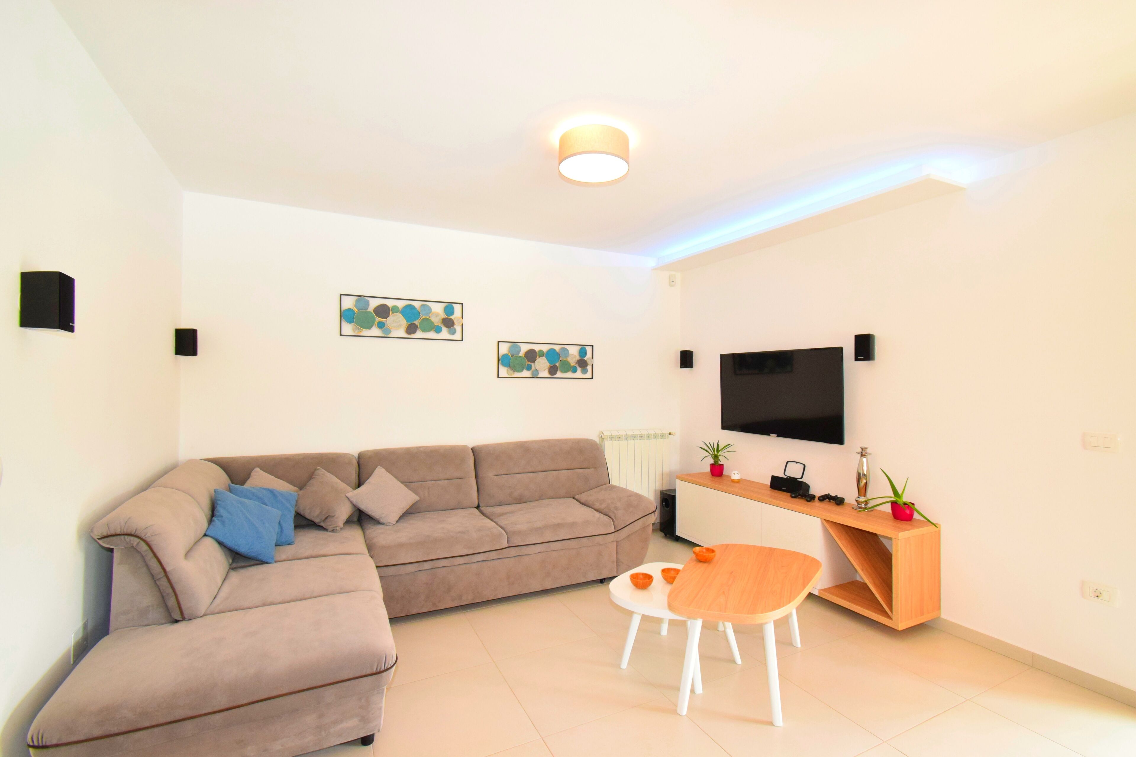 A modern living room with a sectional sofa, a wooden coffee table, and a flat-screen TV mounted on the wall.