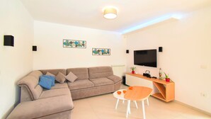 Un salon moderne avec un canapé d’angle, une table basse en bois et un téléviseur à écran plat fixé au mur.