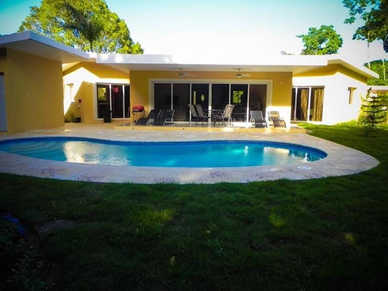 Une maison moderne dotée d’une piscine, d’un patio couvert avec des chaises et d’une pelouse bien entretenue.