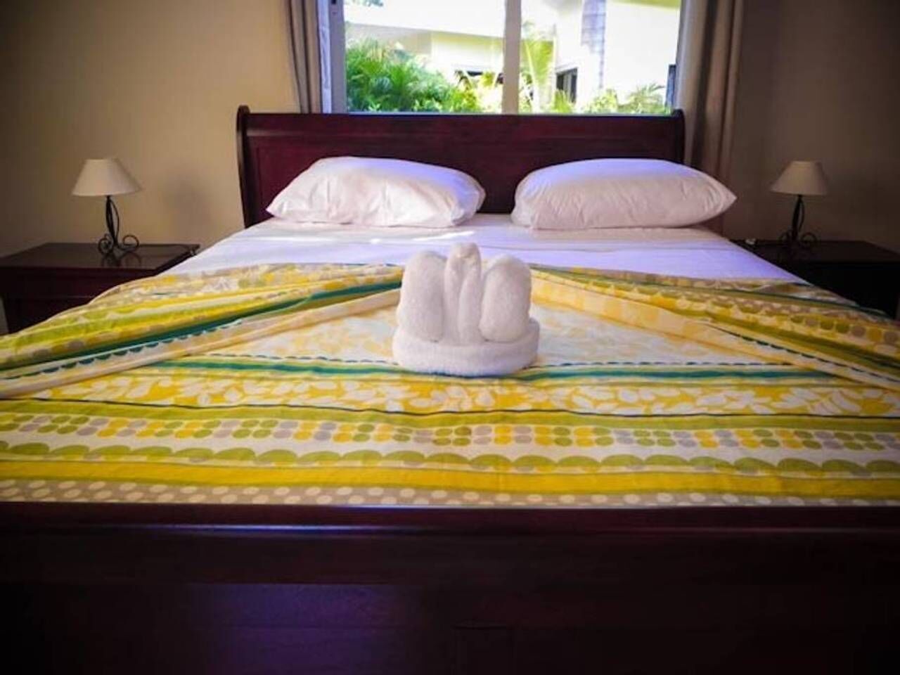 A neatly made bed with a patterned bedspread, two pillows, and a towel arranged in a swan shape on the bed.