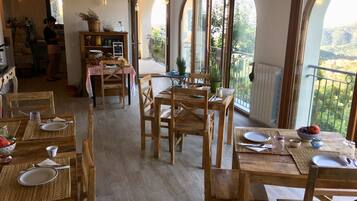Un comedor con mesas y sillas de madera, una cocina al fondo y ventanas amplias con vistas al exterior.