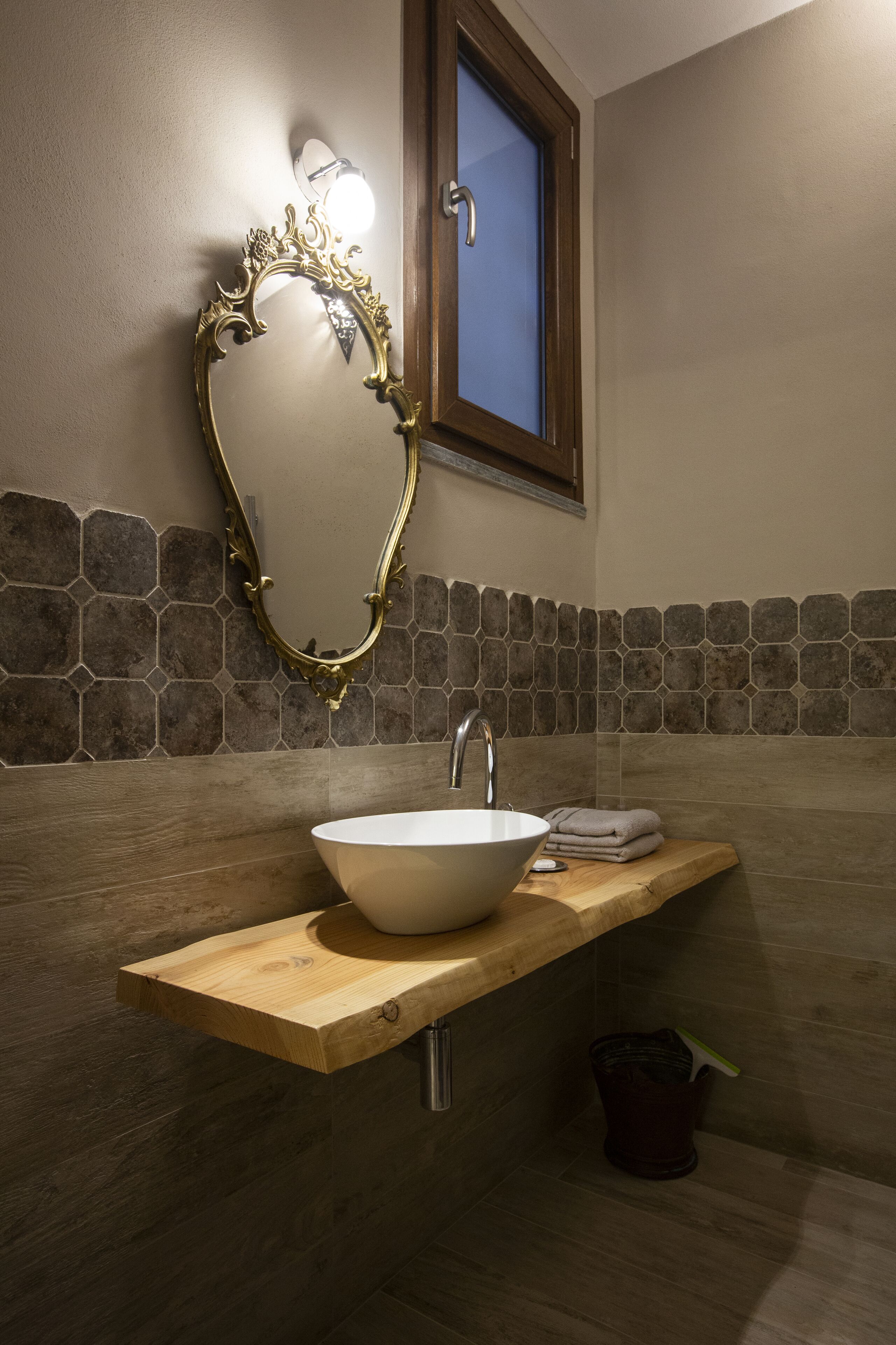 A bathroom with a stone mosaic backsplash, a wooden vanity, a white sink, and a mirror with an ornate frame.