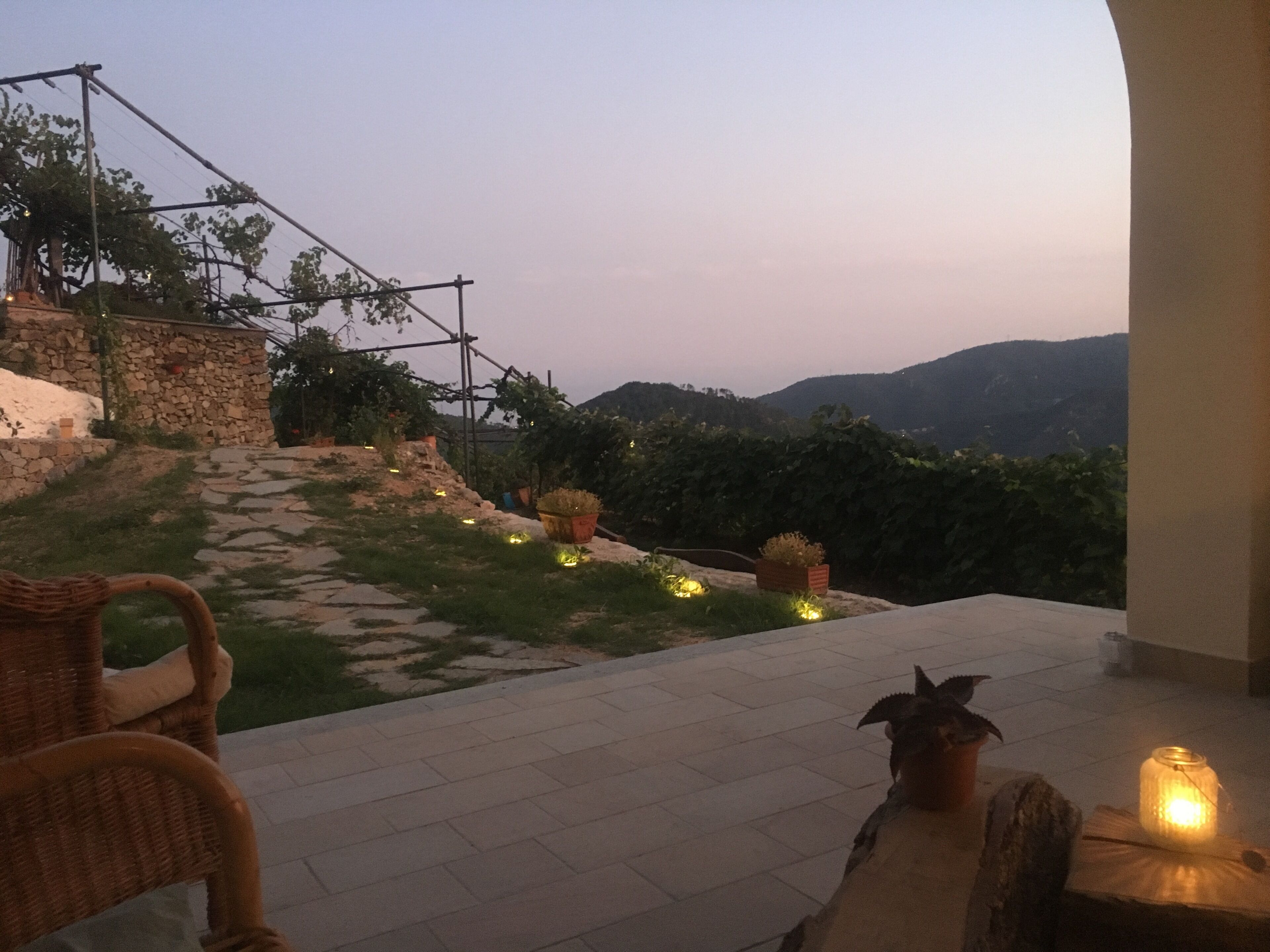 A terrace with a wicker chair, potted plants, and a lit candle.