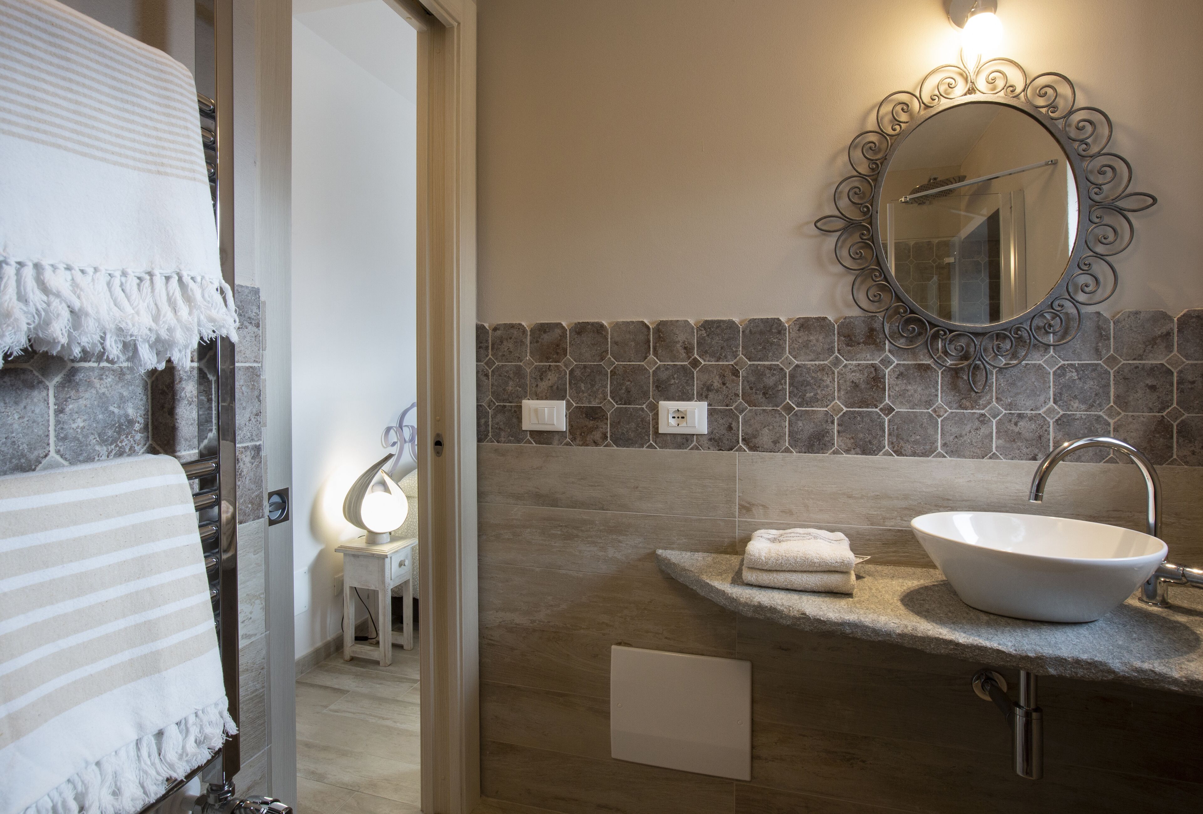Un baño con pared de baldosas de piedra, un lavamanos blanco, un espejo con marco decorativo y un perchero.