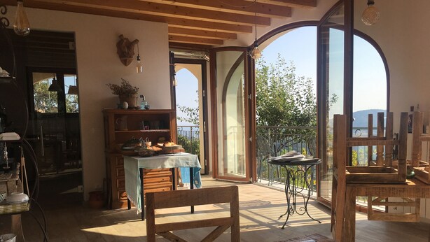 A cozy dining area with wooden furniture, a table with a smartphone, and a view of the outdoors through large windows. - Agriturismo LaValleggia (Tovo San Giacomo)