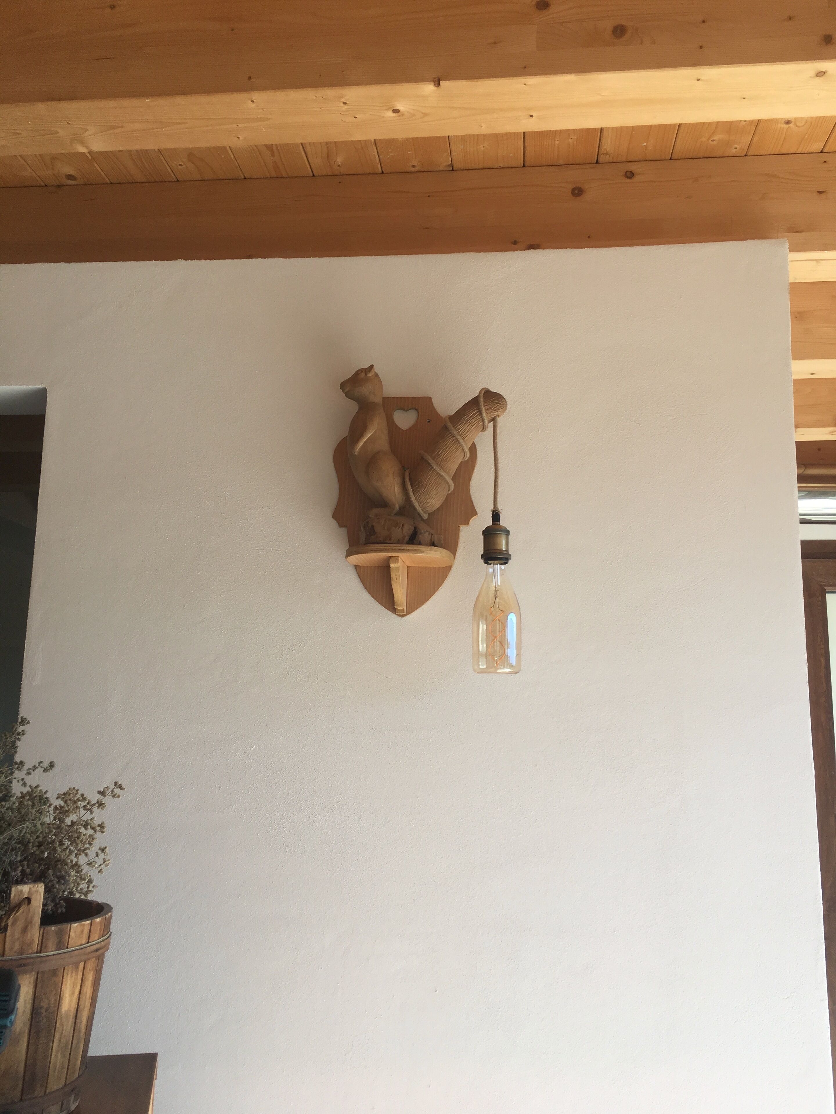 Un luminaire mural au design rustique, comprenant une figurine d’ours en bois et une lampe suspendue.