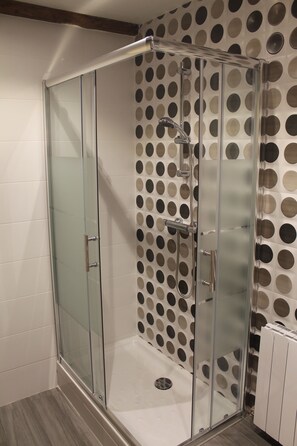 Um chuveiro envidraçado com design moderno, parede revestida com um padrão de bolinhas e piso branco ladrilhado.