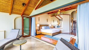 A spacious bedroom with a large bed, a sitting area with a chair and table, and a sliding glass door leading to a balcony. - Stylish Split-Level Condo with a Shaded Terrace, Direct Beach Access, and Resort (Playa Flamingo)