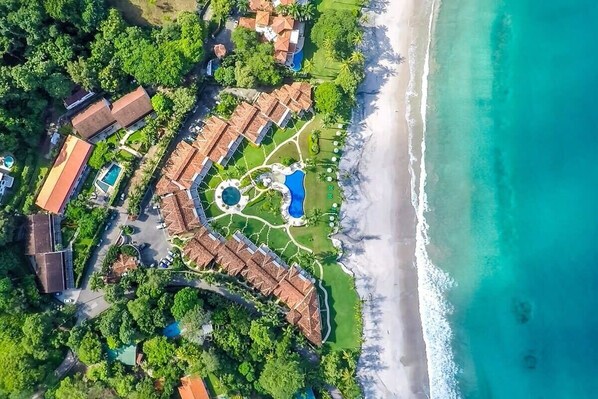 An aerial view of a resort with multiple buildings, a central pool area, and a beach.