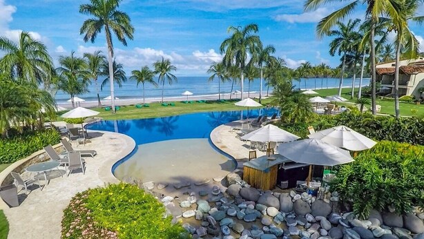 A resort pool area with lounge chairs, umbrellas, and a view of the beach. - Stylish Split-Level Condo with a Shaded Terrace, Direct Beach Access, and Resort (Playa Flamingo)