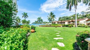 A well-maintained lawn with stepping stones, palm trees, and a view of a beach and ocean. - Stylish Split-Level Condo with a Shaded Terrace, Direct Beach Access, and Resort (Playa Flamingo)