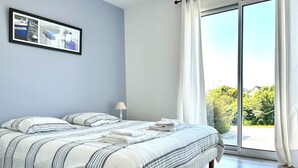 Un dormitorio con cama, mesita de noche, lámpara y ventana con cortinas.