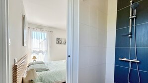 Un dormitorio con cama, mesita de noche, lámpara y vistas al baño con ducha.