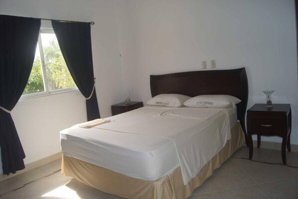 A bedroom with a bed, two bedside tables, a window with curtains, and a nightstand.