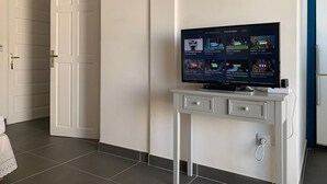 Huoneessa on valkoinen tv-taso, televisio, ovi ja laattalattia.