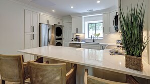 A modern kitchen with white cabinetry, a stainless steel refrigerator, a built-in oven, and a large island with chairs. - 4th Row from the beach! 2 Bed/2 Bath Townhouse (Hilton Head Island)
