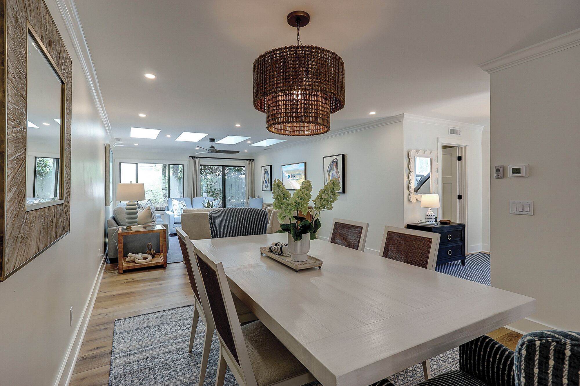 A modern dining area with a large table, chairs, a chandelier, and a view of the living room.