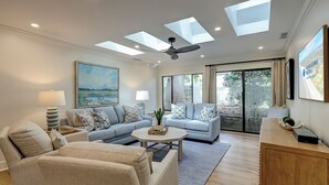 A spacious living room with a ceiling fan, a large window, and a flat-screen TV. - 4th Row from the beach! 2 Bed/2 Bath Townhouse (Hilton Head Island)