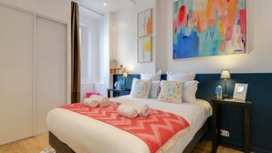 A hotel room with a large bed, a bedside table, a nightstand, a mirror, and a colorful abstract painting on the wall. - Sweett | Clery - Two Bedroom Apartment, Sleeps 4 (Paris)