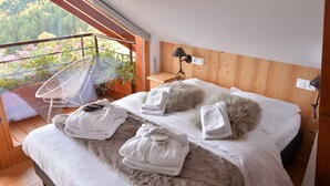 Un dormitorio con una cama grande, cabecera de madera, mesita de noche, lámpara y vistas a un balcón con plantas.