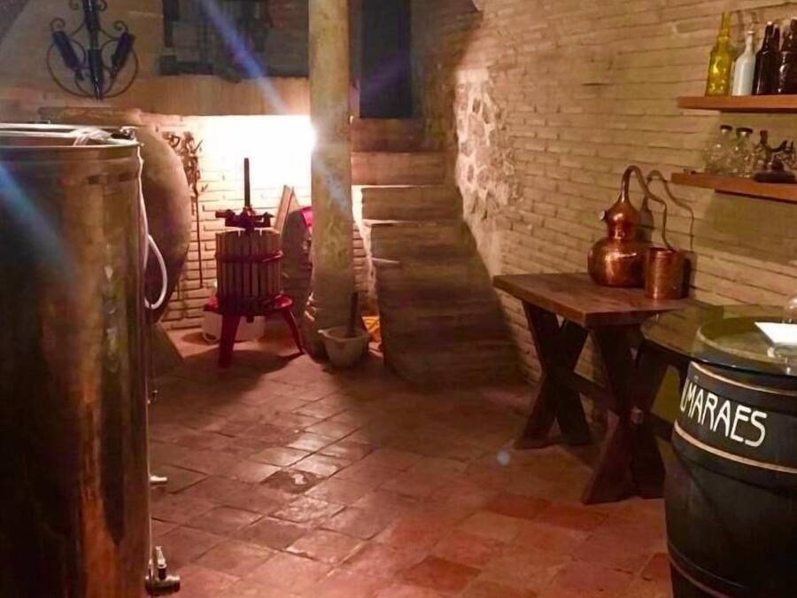 Una bodega rústica con paredes de piedra, una mesa de madera y grandes barriles metálicos.
