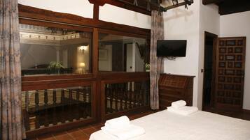 A hotel room with a large bed, wooden balcony, a television mounted on the wall, and a wooden wardrobe.