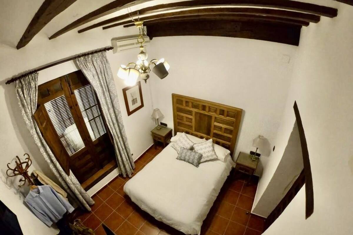 A bedroom with a wooden headboard, a bed with white bedding, a nightstand with a lamp, and a window with blinds.