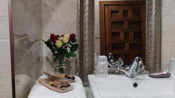 Un baño con un lavamanos blanco, un espejo con marco decorativo, un perchero con toallas dobladas y un florero con flores.