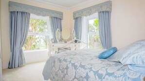 A bedroom with a bed, a dresser, a mirror, and two windows with curtains. - Altahammond House (Carrickfergus)