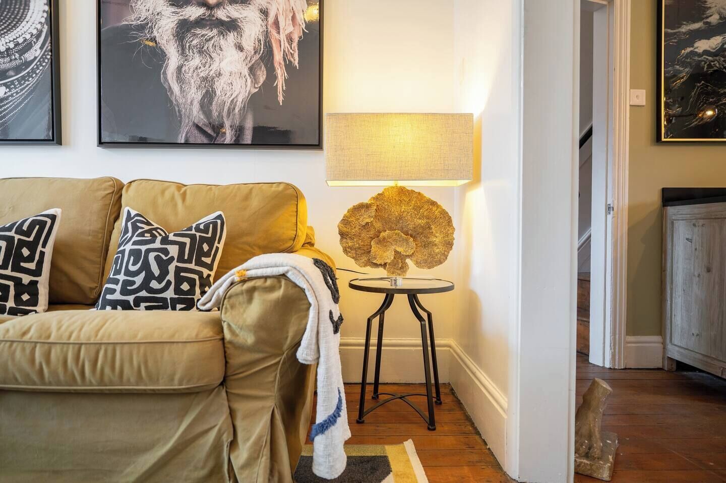 Ein Wohnzimmer mit einem beigen Sofa, einem runden Tisch mit einer Lampe und gerahmten Kunstwerken an der Wand.