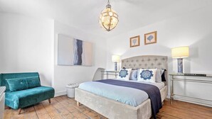 A bedroom with a large bed, a tufted headboard, two bedside lamps, a tufted armchair, a small round ottoman, a framed abstract painting, and a chandelier. - This house is a 4 bedroom(s), 3 bathrooms, located in Manchester, England. (Manchester)