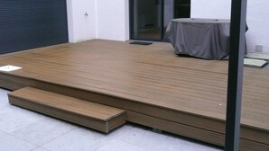 Een houten terras met een tafel, stoelen, een schuifdeur en een garage.