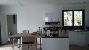 Een moderne keuken met een eethoek, met een houten tafel, barstoelen en een raam met uitzicht op groen.