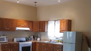 A kitchen with wooden cabinets, a stove, a microwave, a refrigerator, and a window with curtains. - Casita El Sol, Pool View. (Loreto)
