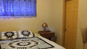 A bedroom with a bed, a nightstand, a lamp, a window with curtains, and a door. - Casita El Sol, Pool View. (Loreto)