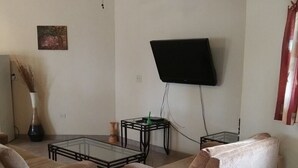 A living room with a ceiling fan, a flat-screen TV mounted on the wall, a glass coffee table, two sofas, and an air conditioning unit. - Casita El Sol, Pool View. (Loreto)
