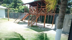 Eine hölzerne Spielanlage mit Rutsche und Treppe, umgeben von einem Zaun und Palmen.